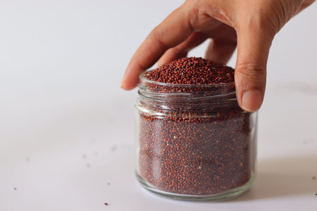 Red quinoa seeds in a glass jar held in hand. Nutritious whole grain rich in protein and fiber. Gluten free plant based superfood ideal for salads, bowls, meal prep and healthy cookingの写真素材