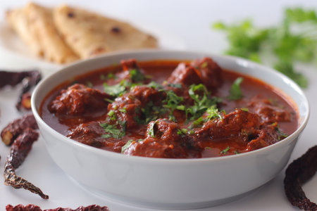 Chicken vindaloo curry served in a bowl with rich spicy red chili gravy, garnished with fresh...