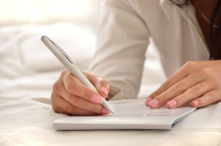 Close up of a young woman in a white scene writing on a pad.