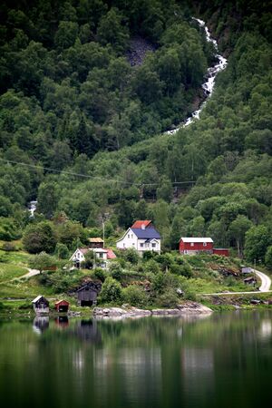 Houses on banks of Lusterfjord with waterfall, near Skjolden, Norway