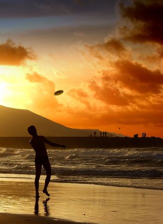 A man throws a frisbee in the ocean on an  beach at sunsetの写真素材