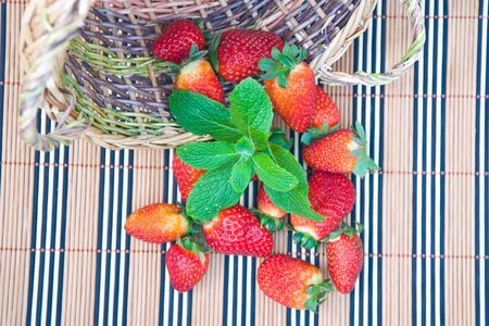 red strawberry and green mint leaves over bamboo tableclothの写真素材