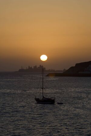 sailboat on beautiful sunset with town at back