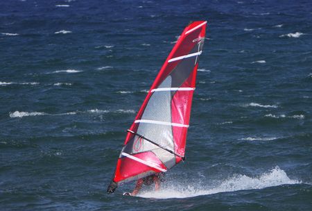 windsurfer sailing away form the beach on blue watersの写真素材