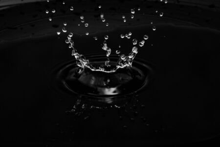 isolated water of drop on black surface with splashの写真素材