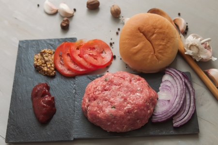 raw hamburger on a wooden board with spices and burger bunの写真素材