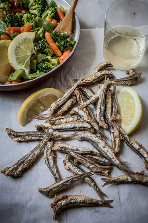 a few deep fried anchovies with lemon and vegetablesの写真素材