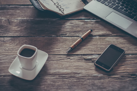 vintage composition of modern wooden table desk with smartphone laptop and cup of coffee with focus on pen and small DOFの写真素材