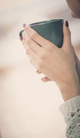 woman in a window with a cup of tea on her handsの写真素材