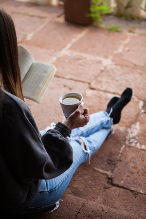 woman reading a book with a cup of  black tea with jeansの写真素材