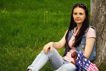 young beautiful woman sitting near a tree on the grass in the park
