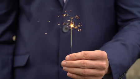 Young businessman in blue suit holds a bengal fire in his hand.の写真素材
