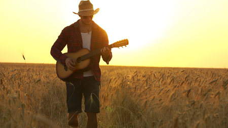 young guy walks the golden wheat field in the rays of the sunset and plays the guitar.の写真素材