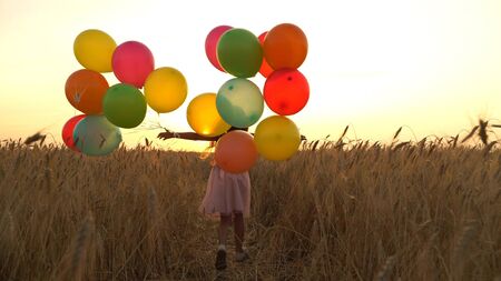 girl walking in a field with balloonsの写真素材