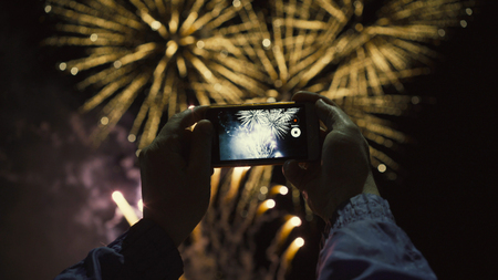 Silhouette of a man photographing fireworks at night sky. Beautiful salute in honor of the holiday.