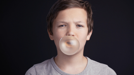 boy make bubble with chew on dark backgroundの写真素材