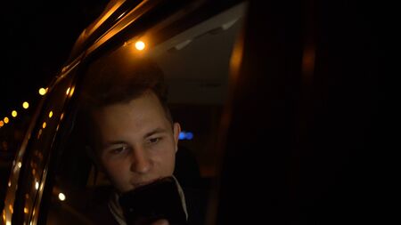 teenager using app on his phone on late night in backseat of car