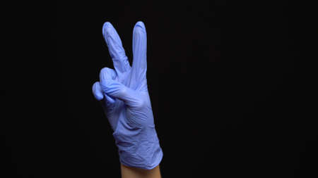 Female hand in a latex medical glove makes an peace gesture isolated on black background