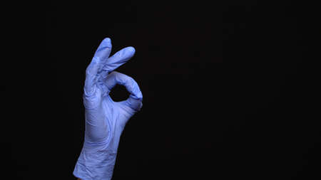 Female hand in a latex medical glove makes an ok gesture isolated on black background
