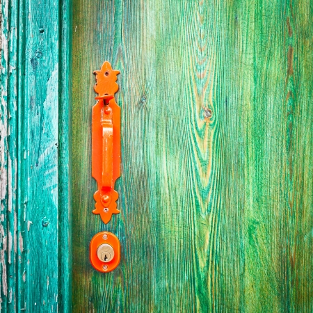 Vibrant orange door handle on a green wooden doorの写真素材