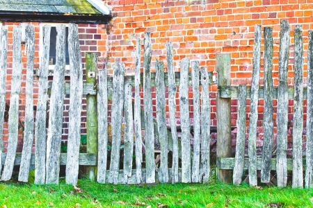 An old wooden picket fence against a red brick wallの写真素材