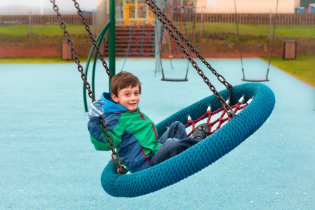 A happy young boy playing on a park swingの写真素材