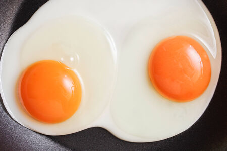Two fresh eggs being fried in a non-stick panの写真素材