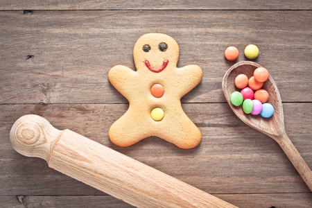 A single gingerbread man on a wooden surface with candy on a spoon and a rolling pinの写真素材