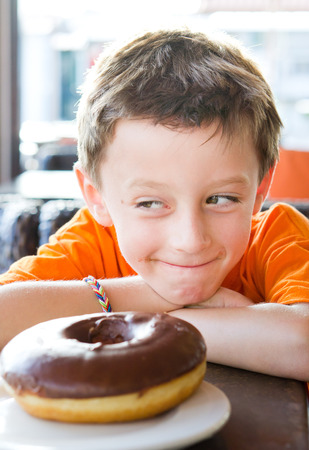 A young boy looking at a chocolate donutの写真素材