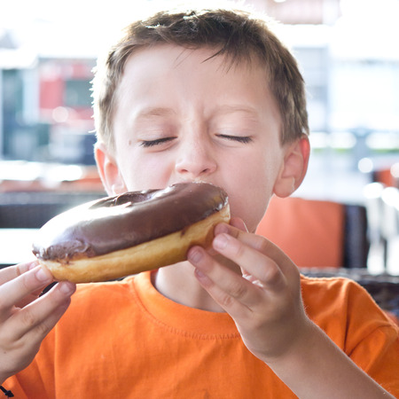 A young boy eating a chocolate donutの写真素材