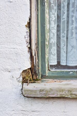 A wooden window frame showing peeling paint and wood rotの写真素材