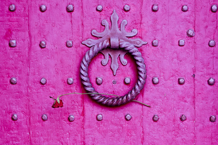 Knocker on a red medieval wooden door with a rose placed in itの写真素材