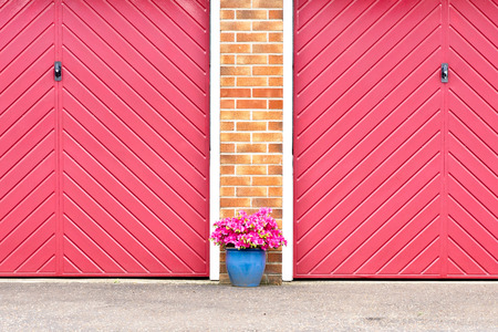Pot of pink flowers in front of red garage doorsの写真素材