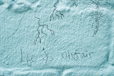 Pencil marks and a slogan stating life is unfair, on a brick wallの写真素材