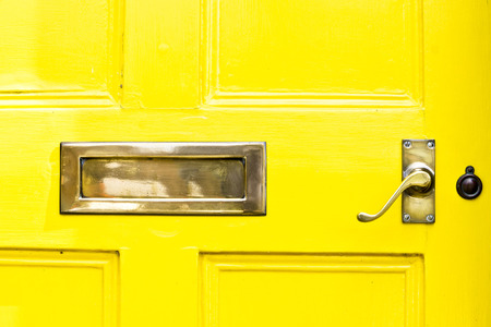 A yellow front door with a metal letterbox and handleの写真素材