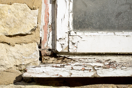 Part of the white wooden frame of an old window with peeling paint and rotten woodの写真素材