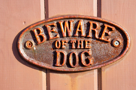 A rusty metal sign on a wooden surface, warning about a dogの写真素材