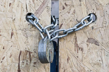 A strong padlock and chain on a plywood gateの写真素材