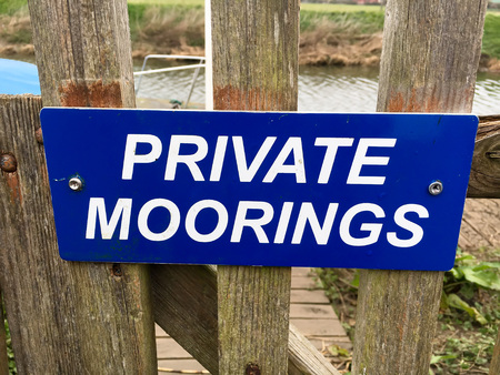 A blue and white sign for private moorings on a wooden fenceの写真素材