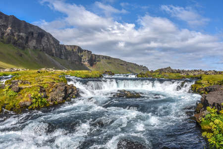 Landscape with little waterfall, green grass and mountains