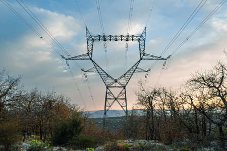 High voltage electric line stretching between the mountain peaks during the setting sunの写真素材