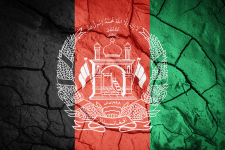 Flag of Afghanistan. Afghanistan symbol. Flag on the background of dry cracked earth. Afghan flag with drought conceptの写真素材