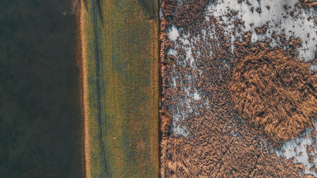 Sunset over a frozen lake. Sunbeams falling on water. Shadows of trees on the ice covering the lake. Aerial view of a frozen lake. Ice sheet background. Frozen grass in waterの写真素材