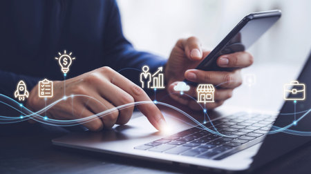 Businessman using mobile phone and laptop with digital business icons on screen.の素材