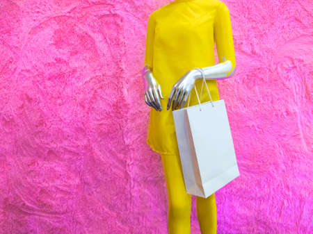 Sale. A mannequin, painted in silver paint and wearing a yellow dress, holds unnamed white paper bags. A mannequin against the background of a purple fur wall.の写真素材