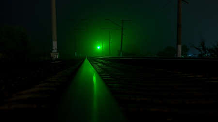 Empty railroad at night. Green traffic lights. A strong wind shakes the treesの写真素材