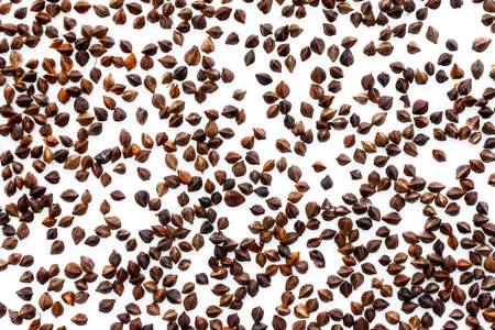 A background of unpeeled whole buckwheat seeds placed on a white background at a short distance from...