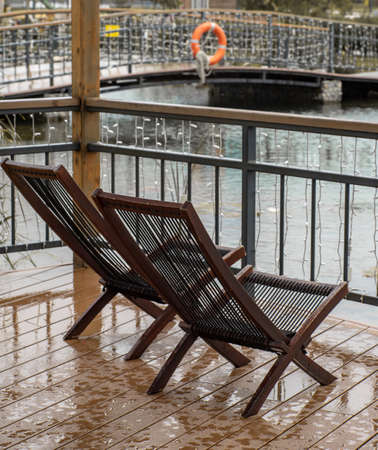 Two chairs on a wet terrace in the rain. Terrace with a pond in autumn.の写真素材