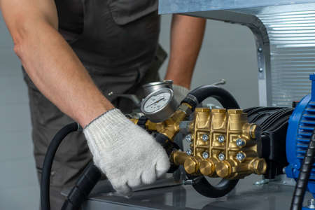 A man's hand in a white glove turns on a set with a pressure gauge for testing high pressure hydraulic hoses. A man in uniform is testing high pressure hoses. Pipe testing system.の素材 [FY310172938330]