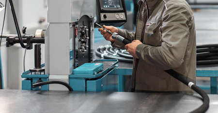 A worker crimps a high pressure hydraulic hose on the machine. High pressure hydraulic hose manufacturing process.の写真素材